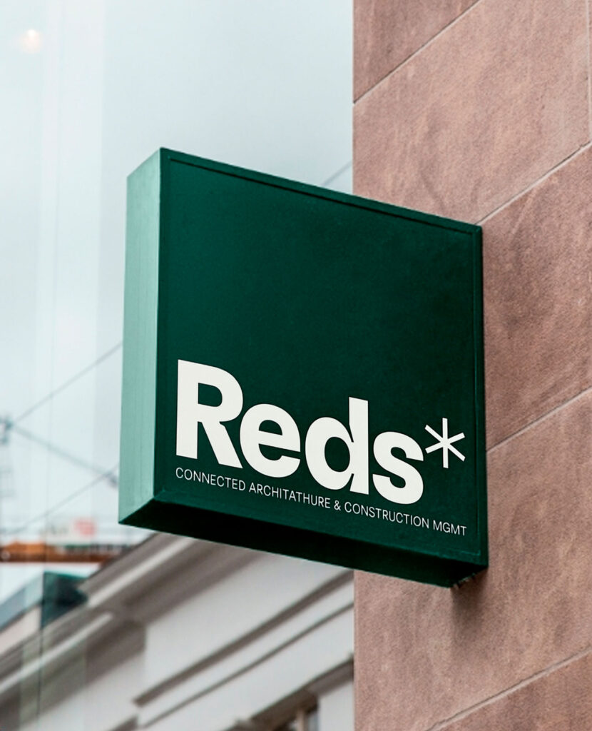 Rótulo verde de Reds en una fachada de ladrillo